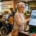Ältere Frau nutzt ein barrierefreies Self-Service-Terminal im Supermarkt, während weitere Kunden unterschiedliche digitale Einkaufslösungen verwenden.