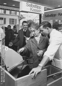 Das Bild aus der Geschichte des Self-Checkouts zeigt die Einweisung einer Kundin in die Bedienung einer Selbsttipp-Kassen in der Migros Testfiliale im Jahr 1965.
