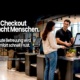 Ein SCO-Attendant unterstützt eine Kundin an einer Self-Checkout-Kasse. Text im Bild: „Self-Checkout braucht Menschen. Ohne gute Betreuung wird aus Komfort schnell Frust.“
